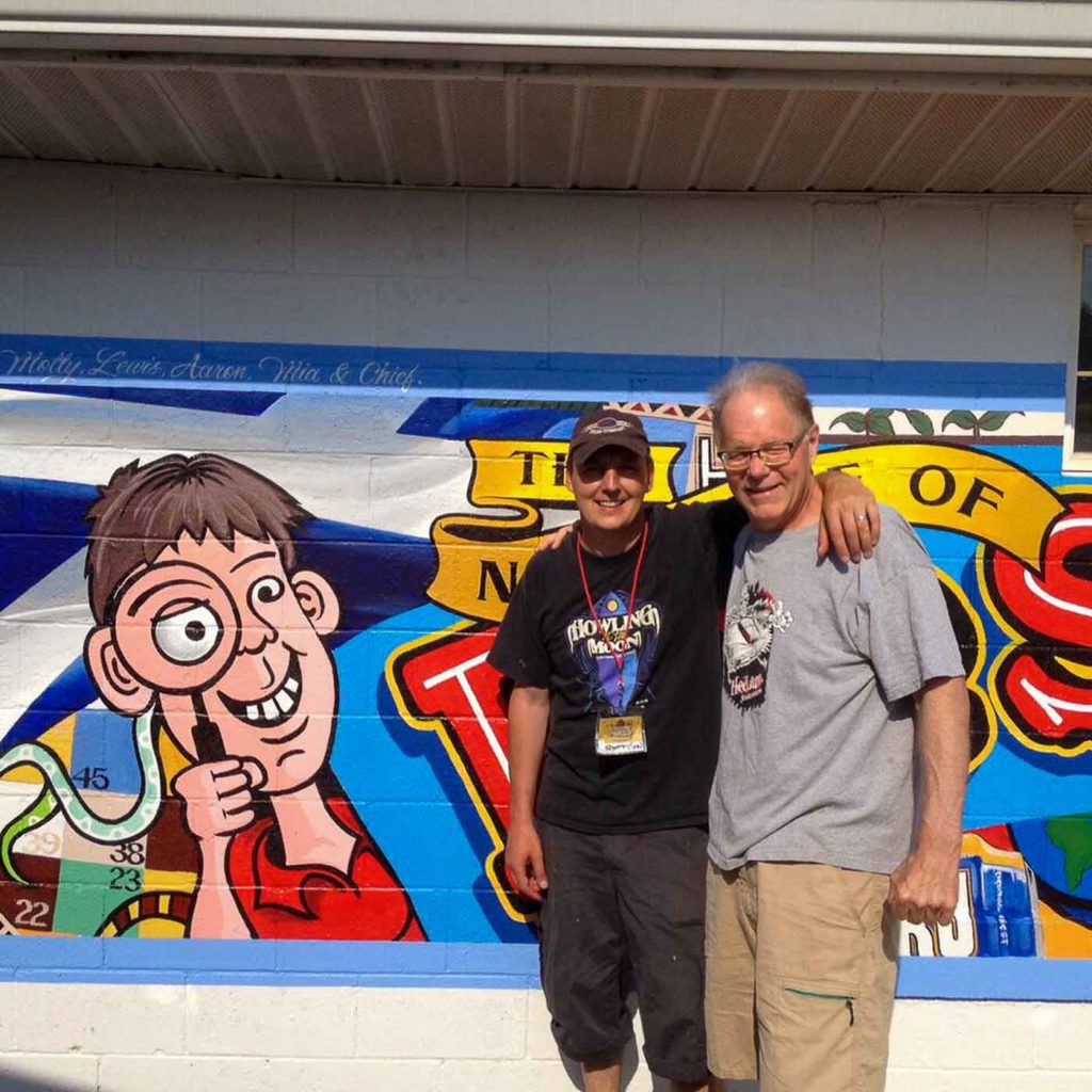 Jeff and friend standing in front of Eye Spy mural on side of building
